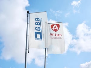 GSB- und ARTUS-Fahnen wehen vor blauem Himmel mit Wolken